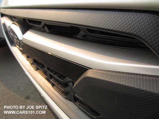 closeup of the 2018 Subaru Crosstrek 2.0i and Premium model front grill showing the  satin top half of the center accent bar, and gloss black lower half, with center logo