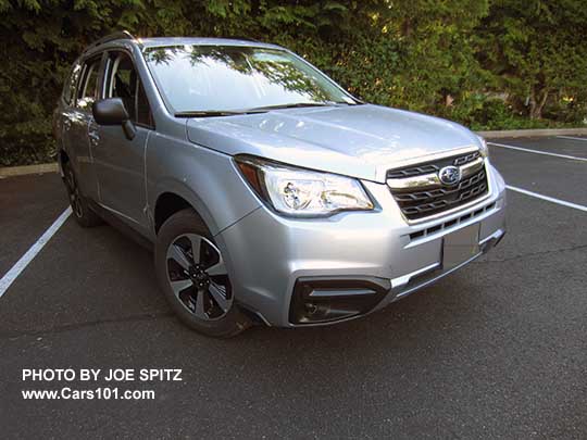 2018 and 2017 Subaru Forester 2.5 base model has unpainted black outside mirrors, and no chrome fog light trim, no dark tinted rear windows, and no lower chrome fog light trim.  Shown with optional Alloy Wheel/Roof Rail Package. Ice silver shown.. Redesigned wheels for 2017