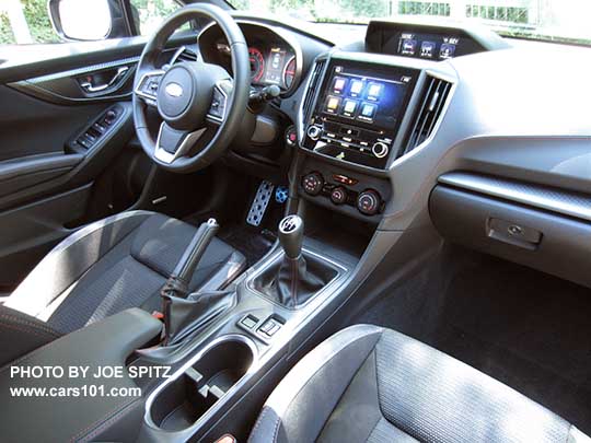 2017 Subaru Impreza Sport manual transmission interior from the passenger side, black sport cloth with red stitching, 8" audio, heated seat buttons, large upper console color trip computer, patterned passenger side dash trim.
