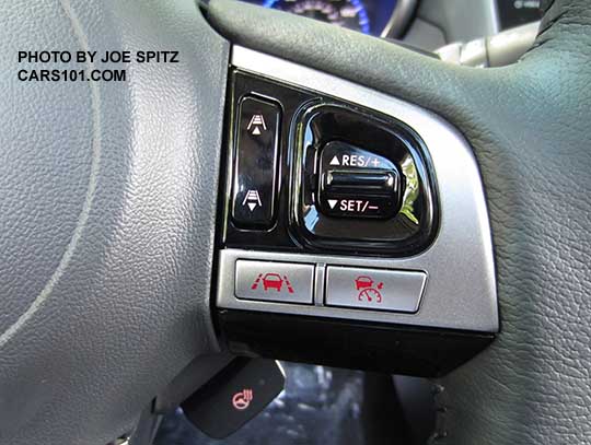 closeup of the 2017 Outback Touring gray leather wrapped steering wheel's gloss black and silver fingertip controls. Right side shown with Eyesight cruise controls, and lane keep assist. The silver buttons are red lit because the headlights are, otherwise they are black. The Touring model steering wheel is heated and that is the lower button