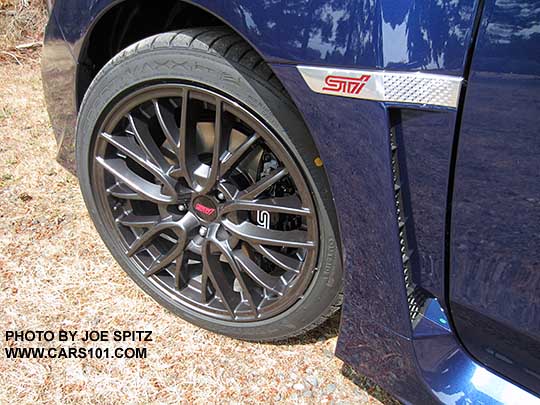 2016 Subaru STI 18" gray multi-spoke alloy wheel and front fender with STI emblem on a Lapis Blue car