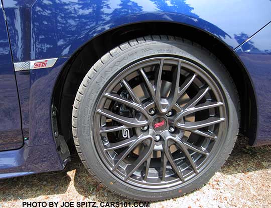 2016 Subaru STI 18" gray multi-spoke alloy wheel and front fender with STI emblem on a Lapis Blue car, white STI logo on the black front brake caliper