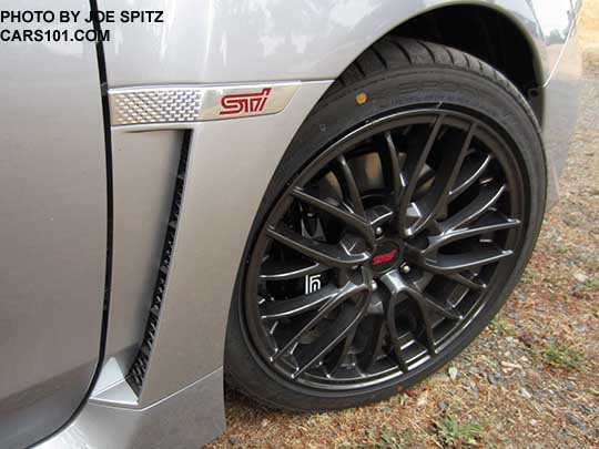 2016 Subaru STI 18" gray multi-spoke alloy wheel and front fender with STI emblem on an Ice Silver car