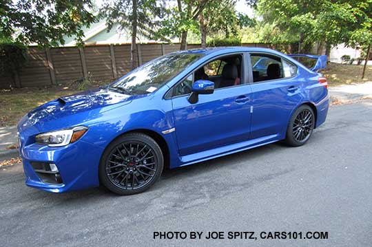 side view 2016 Subaru WRX STI, 18" gray alloy wheels, fog lights, black inner headlight surrounds, tall rear spoiler, WR Blue shown