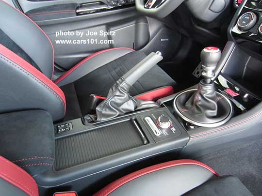 closeup of the 2018 Subaru WRX STI interior- black and red seats, alcantara armrest, red stitching, center console with heated seat buttons, cupholder with sliding cover, DCCD,  SI Drive, gloss black storage with red lit STI logo