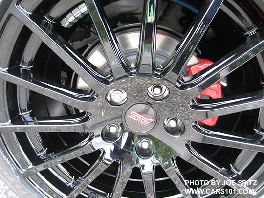 closeup of the 2018 Subaru WRX optional black STI alloy wheel, front wheel shown on a white car. Red brake calipers means this is a Premium with the optional Performance Pkg.