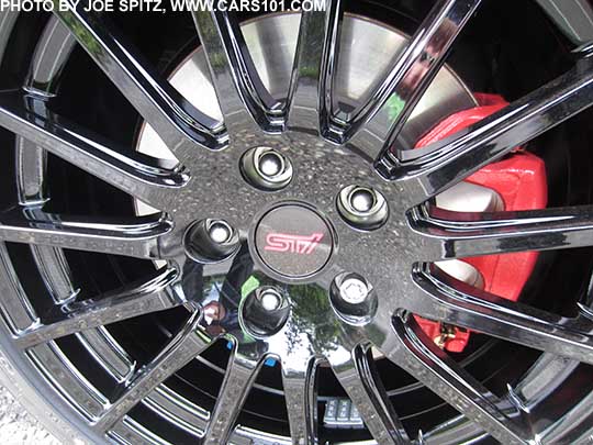 closeup of the 2018 Subaru WRX optional dealer installed black 18" STI alloy wheel, front wheel shown on a white car. Red brake calipers means this is a Premium with the optional Performance Pkg
